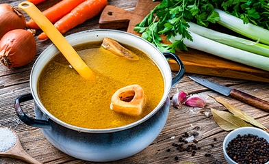 Bowl of soup on table surrounded by vegetables