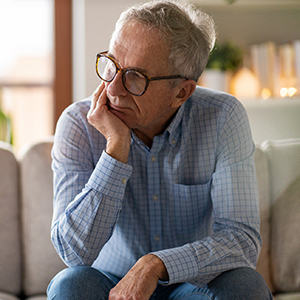 Man seated on sofa, holding chin in hand