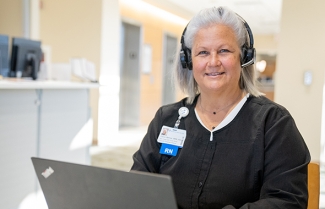 Smiling nurse wearing headset and sitting at computer.