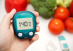 Hand holding glucometer; fresh produce in background