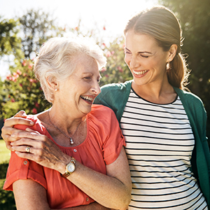 Oldre woman and younger woman walking outdoors, laughing and embracing