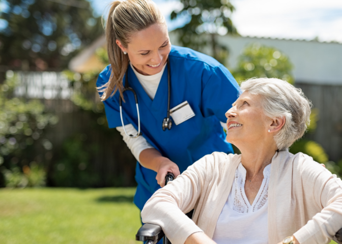 Healthcare provider pushing older woman in wheelchair outdoors 
