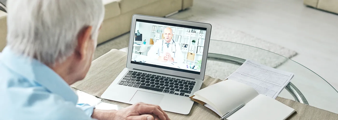 Older man at table, on video call with healthcare provider